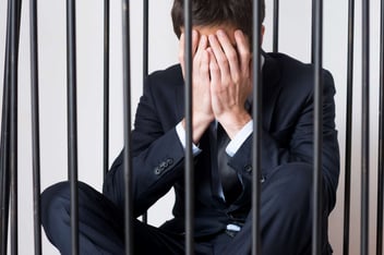 homem de negócios em uma cela com as mãos no rosto representando o compliance criminal